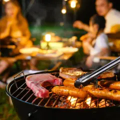 Une famille profite d'un barbecue en soirée. Des saucisses et une côte de porc cuisent sur le gril, la température de cuisson saucisse barbecue est parfaite.