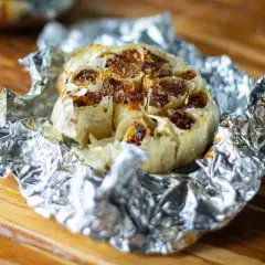 Ail au barbecue, rôti à la perfection dans du papier d'aluminium, prêt à être pressé sur du pain grillé.
