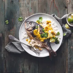 Dorade grise entière, parfaitement cuite, servie avec du riz blanc, une sauce jaune onctueuse, des quartiers de citron vert et de la coriandre fraîche. Un délice visuel pour la cuisson dorade grise.