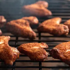 Ailes de poulet marinées pour barbecue, grillées à la perfection, dégageant une fumée alléchante.