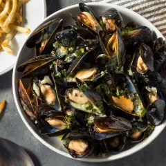 Un plat généreux de moules au feu de bois, parsemées d'herbes fraîches et servies avec des frites croustillantes.