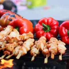Brochettes de poulet et poivrons rouges sur un barbecue, éclairés par la lumière des flammes.