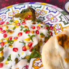 Un plat de mutabal crémeux, garni de grenades et de pignons, servi avec du pain pita sur une assiette décorée.