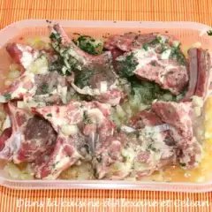 Côtelettes d'agneau crues dans une marinade à l'oignon et aux herbes, prêtes pour une recette de marinade agneau barbecue.