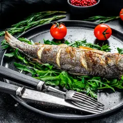 Poisson entier au barbecue, servi sur un lit de roquette avec des tomates cerises et des herbes.