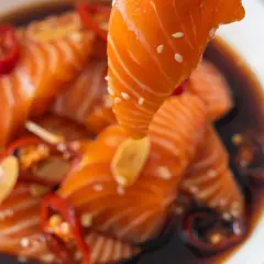 Un morceau de saumon est soulevé d'une marinade foncée avec des piments rouges et de l'ail. Parfait pour une marinade poisson plancha.
