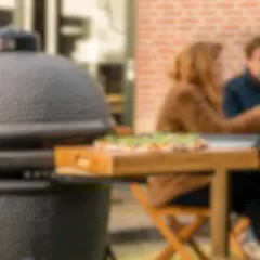 Un couple profite d'un repas en plein air avec une pizza sur une planche en bois à côté d'un barbecue kamado.