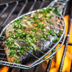 Poisson entier assaisonné d'herbes et d'épices, sur une grille de barbecue avec des flammes vives. Le temps de cuisson du poisson au barbecue est crucial pour un résultat parfait.