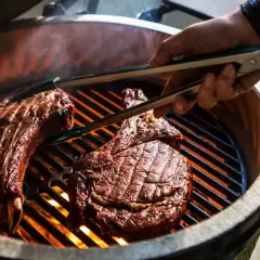 Deux côtes de bœuf savoureuses sur un barbecue à gaz, prêtes pour le temps de cuisson idéal. La chaleur intense des flammes caramélise la viande.