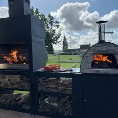 Un grand barbecue et un four à pizza en pierre sont prêts à preparer barbecue. Le feu crépite dans les deux, promettant un repas convivial en plein air.
