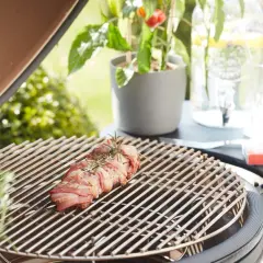 Un rôti de viande enroulé de lard, prêt à griller. Une légère **fume bleu** s'échappe, promettant un repas savoureux en plein air.