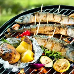 Trois poissons maquereaux grillés sur un barbecue, accompagnés de pommes de terre en papillote, de tomates et de citrons. Un délice de poisson barbecue en plein air.