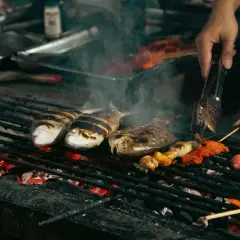 Poissons et brochettes marinés cuisent sur un gril incandescent, dégageant une fumée alléchante. Un vrai bar au barbecue !