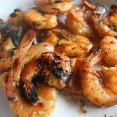 Grosses crevettes bbq, grillées à la perfection, avec des marques de cuisson foncées et une sauce savoureuse.
