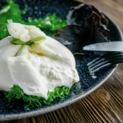 Une burrata fumée onctueuse sur un lit de verdure, prête à être dégustée. Une recette simple et savoureuse.