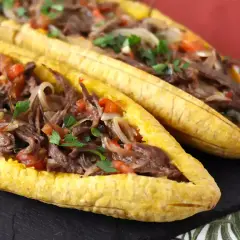 Deux bananes plantain farcies d'un ragoût de bœuf effiloché, d'oignons et de tomates, garnies de persil frais.