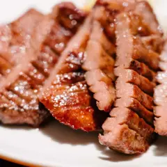 Tranches de langue de bœuf grillée, tendres et juteuses, servies sur une assiette blanche.
