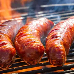 Trois saucisses de bœuf grillent sur un barbecue, leurs jus pétillent sous les flammes. La cuisson saucisse de bœuf barbecue est à son apogée.