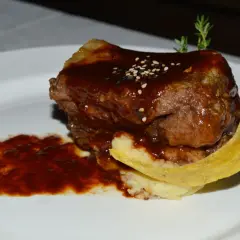 Un plat de ribs de boeuf barbecue, nappé d'une sauce foncée, servi avec une purée et une tranche de banane plantain frite.