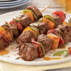 Brochettes de bœuf marinées, garnies de poivrons et tomates, servies sur une assiette blanche.
