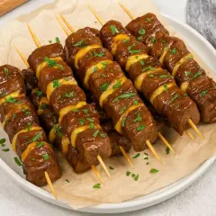Plusieurs brochettes de bœuf et fromage, garnies de persil frais, sont présentées sur une assiette.