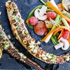 Tentacules de poulpe au barbecue, grillés et garnis d'herbes fraîches, servis avec des légumes croquants et des quartiers de citron grillé.