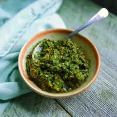 Un bol de pesto de fanes de carottes, prêt à être dégusté, avec une cuillère en argent.