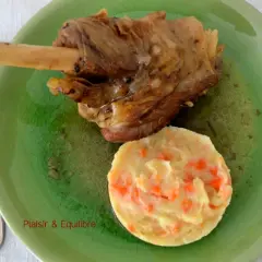 Souris d'agneau confite, tendre et savoureuse, servie avec une purée de carottes onctueuse sur une assiette verte craquelée.