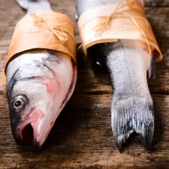 Deux poissons prêts pour le barbecue, emballés dans du papier kraft sur une table en bois rustique.