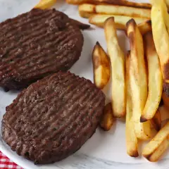 Deux steaks hachés au grill électrique, marqués de fines rayures, accompagnés d'une généreuse portion de frites dorées et croustillantes.