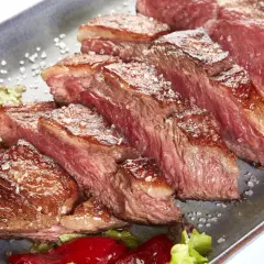 Tranches de picanha de veau juteuse, saupoudrées de gros sel, servies avec des poivrons rouges et de la laitue.