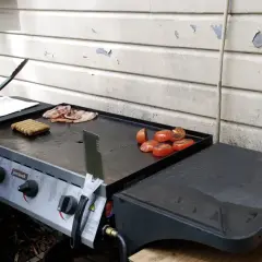 Comment allumer plancha gaz : des saucisses, du bacon et des tomates grillent sur la plaque.