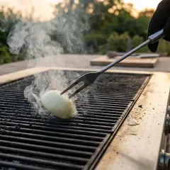Une main gantée utilise une fourchette pour retourner un oignon sur un grill chaud, une astuce pour comment nettoyer un grill viande.