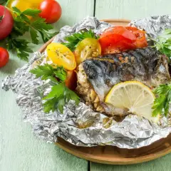 Poisson barbecue en papillote, servi avec des tomates et du persil, garni d'une tranche de citron.