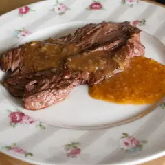 Un plat de viande tendre nappé d'une sauce onctueuse à l'échalote, servi sur une assiette à motifs floraux.