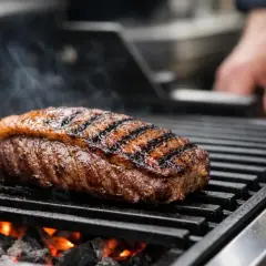 Une picanha de cochon juteuse grésille sur un barbecue, avec des marques de grill parfaites et de la fumée s'élevant.
