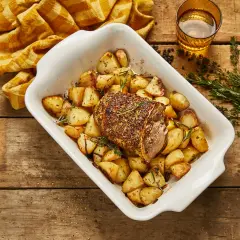 Selle d'agneau rôtie avec pommes de terre dorées et herbes aromatiques dans un plat blanc, prête à être dégustée.