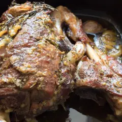 Une succulente épaule d'agneau confite, dorée et parfumée, baignant dans son jus avec des herbes et de l'ail.