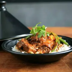 Un plat de riz blanc garni d'un ragoût de bœuf savoureux, aux haricots verts et coriandre, servi à côté d'un tajine noir. La marinade boeuf a conféré une sauce riche et appétissante.