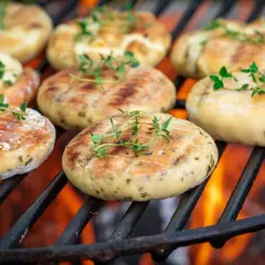 Ronds de halloumi au barbecue, dorés et parsemés de thym frais, grésillant sur les braises ardentes.