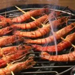 Gambas grillées sur un barbecue, fumantes et appétissantes. Une bouteille de sauce est à proximité, suggérant une délicieuse marinade pour gambas au barbecue.