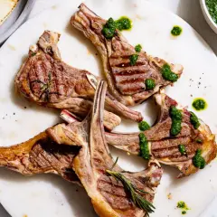 Délicieuses côtelettes d'agneau barbecue, grillées à la perfection, arrosées d'une sauce verte vibrante et garnies de romarin frais.