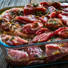 Morceaux de joue de porc marinés dans un plat en verre, prêts à être cuisinés.