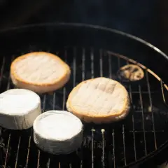 Fromages ronds, dont certains enrobés de blanc, chauffent sur un barbecue. Une idée gourmande pour un barbecue feta.