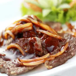 Un steak savoureux nappé d'une sauce brune et d'oignons caramélisés, servi avec une garniture de salade verte.