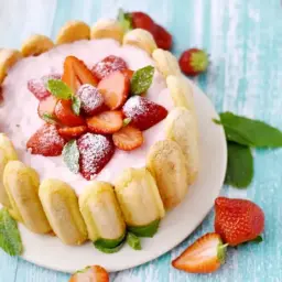 Délicieuse charlotte fraise garnie de fruits frais et de biscuits à la cuillère, saupoudrée de sucre glace.