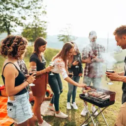 Un groupe d'amis profite d'un barbecue en plein air, une excellente idée pique-nique. Ils tiennent des verres de vin rouge, savourant la bonne compagnie et la nourriture grillée.