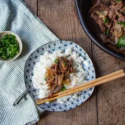 Un plat de riz blanc garni de boeuf aux oignons et de coriandre fraîche, prêt à être dégusté avec des baguettes.
