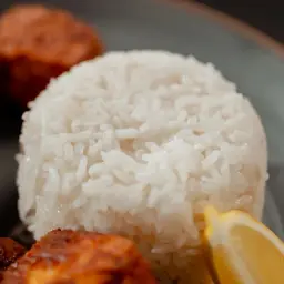 Un monticule de riz thaï parfumé, accompagné de boulettes de viande croustillantes et de quartiers de citron frais sur une assiette grise.