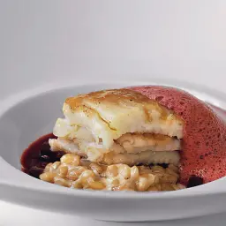 Délicieuse aile de raie poêlée, servie sur un lit de grains perlés, nappée d'une sauce rouge et d'une mousse aérienne.